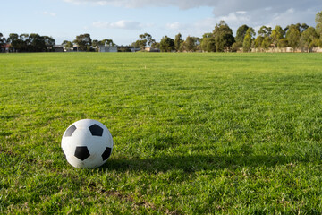 A soccer ball on a large open grass field.  Background texture of a football on a public sports ground with green healthy lawn. Concept of kids activity or community infrastructure. Copy space.