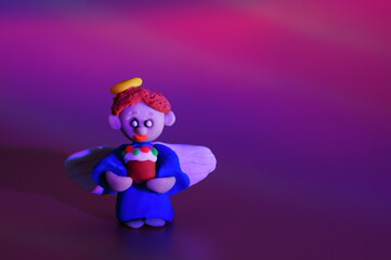 A little angel made of plasticine with a toy Easter. Bright colored background.