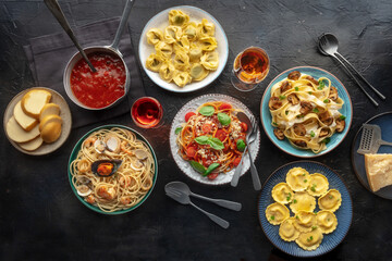 Pasta variety. Italian food and drinks, overhead flat lay shot on a black background. Spaghetti marinara, mushroom pappardelle, seafood pasta, wine