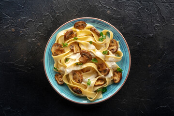 Mushroom pasta, pappardelle with cream sauce and parsley, overhead flat lay shot on a black stone...