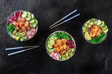 Poke bowl variety. Healthy Hawaiian dish with salmon, tuna, and shrimps, overhead flat lay shot on a black background, with chopsticks and copy space