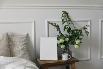 White picture frame mockup and cup of coffee on wooden night stand. White viburnum, fern and...