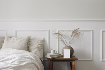 Elegant Scandinavian bedroom interior. Blank greeting card, invitation mockup on bedside table. Cup...