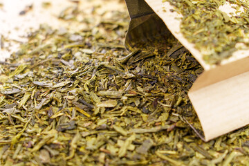 Scattered dried green sencha tea leaves with paper pack