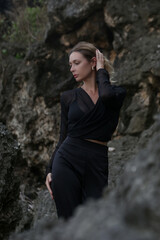 Stylish fashionable model in black outfit posing on rocks sea coast