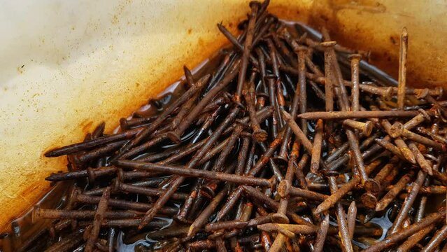 A pile of large rusty iron industrial nails submerged in corrosion-filled water