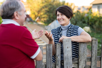 Neighbors standing at fence outdoors and having conversation. Village residents talking