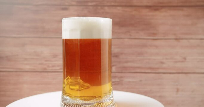 Craft Beer into the large glass. Beer Mug. On a wood background. Half a liter, close up. Rotation 360 degrees. Glass full of beer.