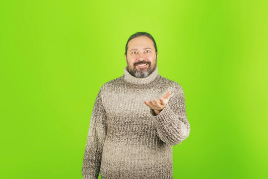 An adult man in a warm sweater on a plain green background. Template with a smiling man and an empty outstretched hand with a place for an object.