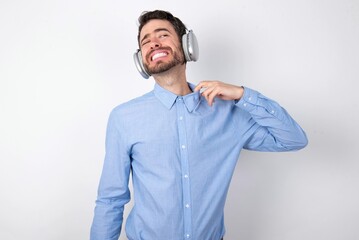 businessman wearing blue t-shirt with headphones over white background stressed, anxious, tired and frustrated, pulling shirt neck, looking frustrated with problem