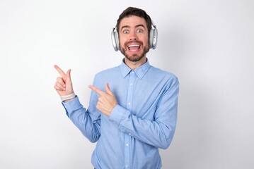 businessman wearing blue t-shirt with headphones over white background points at copy space indicates for advertising gives right direction