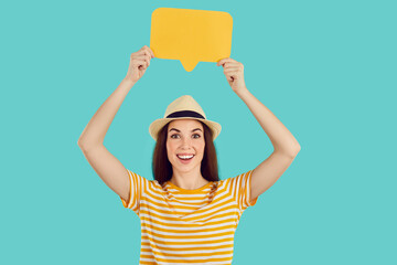 Cheerful young Caucasian woman looking at screen with smile raising yellow dialogue bubble above head for your message wearing striped T-shirt standing in turquoise studio. Idea, wow emotions concept