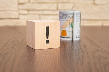 wooden cube with exclamation point and banknotes dollars on wooden table. concept of uncertainty,...