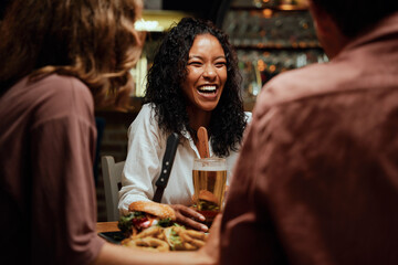 Happy young multiracial group of friends in casual clothing laughing during dinner at restaurant