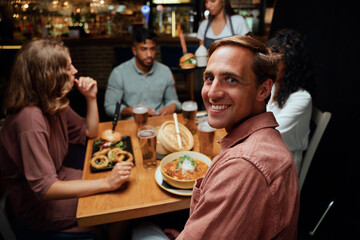 Happy young multiracial group of friends in casual clothing smiling while receiving dinner at bar