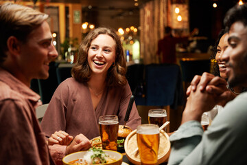 Happy young multiracial group of friends in casual clothing laughing and enjoying dinner at bar