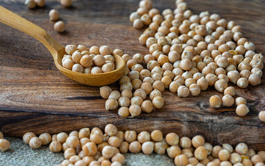 raw chickpeas in a wooden spoon on a rustic wooden cutting board close-up.