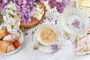 Top view of cup of cappuccino and croissants with strawberry filling on the table with lilac flowers