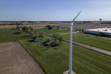 A wind turbine is seen in a field in front of a farm.