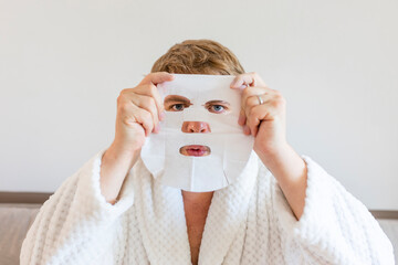 Funny man having fun at home using the face mask for better mood feeling awesome. Portrait of guy doing cosmetic procedures. People skin care concept