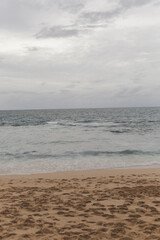 Ocean waves break on empty sand beach during cloudy gloomy day