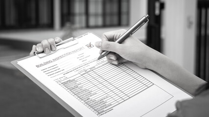 An engineer hand is using a pen checking on the building inspection report form to QC building...