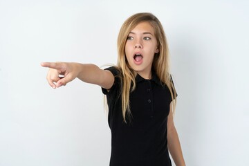 beautiful teen girl wearing black dress over white studio background Pointing with finger surprised ahead, open mouth amazed expression, something on the front.
