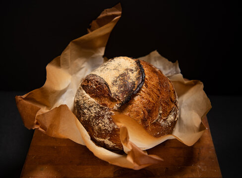 Fresh sourdough bread loaf in browned parchment paper against a black background