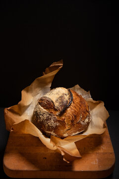 Fresh sourdough bread loaf in browned parchment paper against a black background