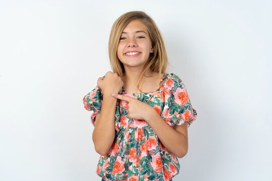beautiful teen girl wearing flowered dress over white studio background In hurry pointing to wrist watch, impatience, looking at the camera with relaxed expression