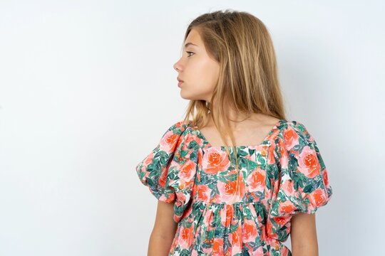 Close up side profile photo of beautiful teenager girl wearing floral dress over white studio background not smiling attentive listen concentrated
