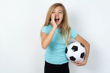 beautiful caucasian teen girl wearing sportswear holding a football ball over white wall shouting excited to front.