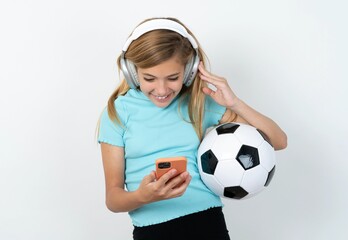 Happy beautiful caucasian teen girl wearing sportswear holding a football ball over white wall...