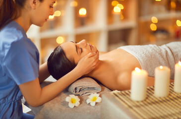 Pretty woman enjoying beauty treatments at a spa salon. Cosmetologist doing a face massage to a relaxed beautiful young lady lying on the spa bed. Relaxation, beauty, skin care concept