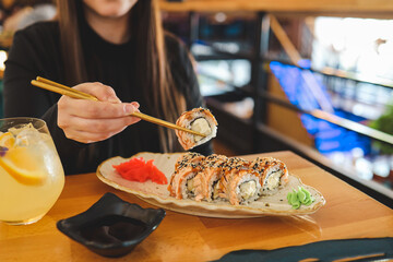 Beautiful young woman eating sushi roll at cafe. Woman eating sushi set with chopsticks on...