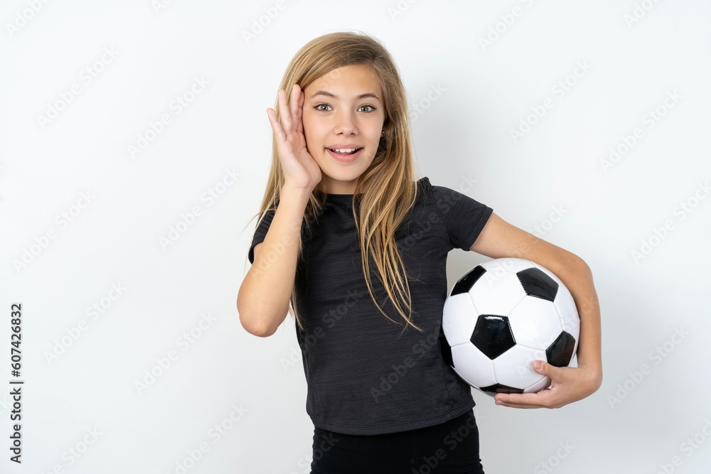 Wall mural beautiful caucasian teen girl wearing sportswear holding a football ball over white wall pleasant lo