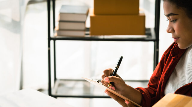 African american woman checking shopping online order on laptop and writing notes on clipboard