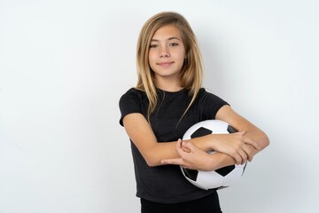 Confident beautiful caucasian teen girl wearing sportswear and football ball over white wall with...