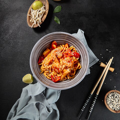 Overhead view of handmade wheat noodles with shrimps and vegetables in sweet chili sauce, on a black background with textile and chopsticks