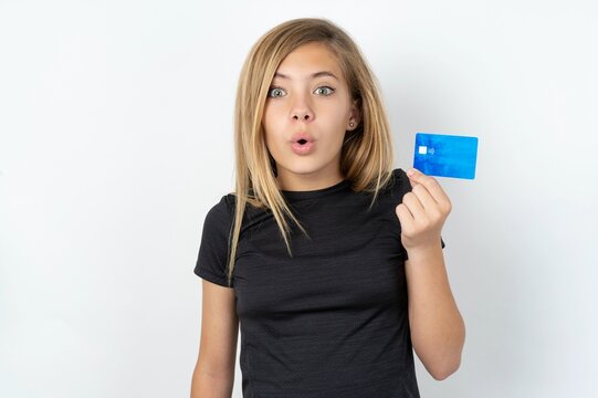 Photo of beautiful caucasian teen girl wearing sportswear  over white wall amazed shocked hold credit card payment