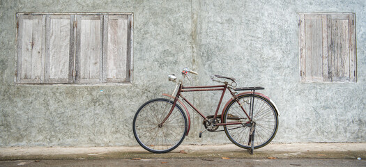 Fototapeta na wymiar Banner panorama size of Vintage bicycle on old rustic dirty wall house, many stain on wood wall. Classic bike bicycle on decay brick wall retro style. Cement loft partition and window background.