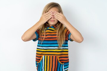 beautiful caucasian teen girl wearing striped T-shirt over white wall covering eyes with both...