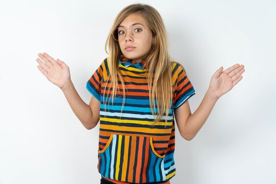 Puzzled and clueless beautiful caucasian teen girl wearing striped T-shirt over white wall with arms out, shrugging shoulders, saying: who cares, so what, I don't know.