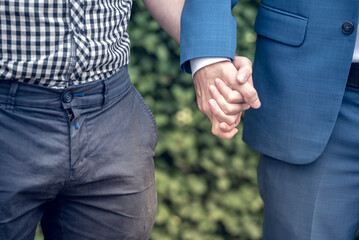 Happy couple LGBT gay in casual suit holding hands looking to each other in park. LGBT gay male couple embrace clasp hand each other