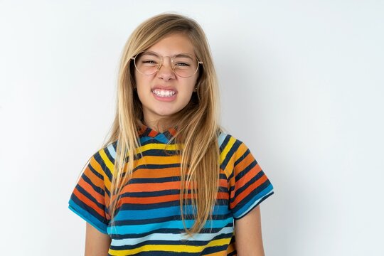 Mad crazy beautiful caucasian teen girl wearing striped T-shirt over white wall clenches teeth angrily, being annoyed with coming noise. Negative feeling concept.