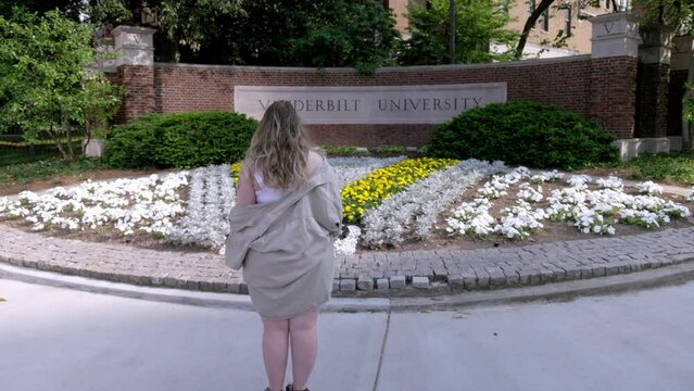 Young college female student walking by the Vanderbilt University sign in Nashville, Tennessee walking behind.