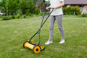 Young woman mowing lawn with a manual push lawn mower - obrazy, fototapety, plakaty