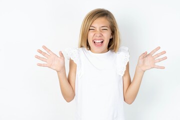 Crazy outraged beautiful caucasian teen girl wearing white T-shirt over white wall screams loudly...