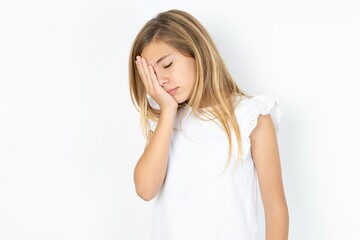 beautiful caucasian teen girl wearing white T-shirt over white wall with sad expression covering...