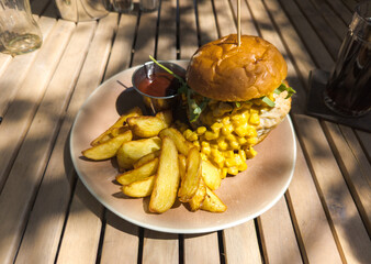 Tasty food on the table in outdoors street restaurant. Burger with fry potato slices, corn and chicken meat.